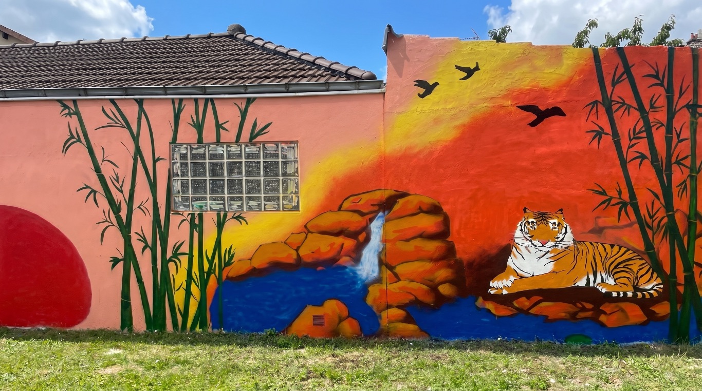 Facade peinte en continu : ciel couchant orange, bambous, cascade entre les rochers, oiseaux en vol et tigre couche, fenetre integree au decor